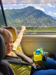Obraz premium A small child sits in a child car seat and looks at the mountains during the trip.