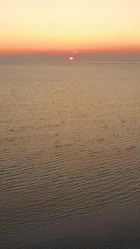 Vertical drone sunrise over Cape Cod tidal flats, soft pastel sky and shimmering bay water with sandbar patterns below. Calm morning coastal b-roll with clean copy space.