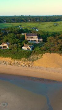 Vertical drone golden hour over Cape Cod shoreline, beachfront houses, sandy bluffs, and winding tidal channels below. Calm coastal neighborhood framed for tall-format aerial b-roll.