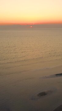 Vertical drone sunrise over Martha&rsquo;s Vineyard coastline, warm sun reflecting on Atlantic water and patterned sandbars at low tide. Serene New England beach dawn b-roll.