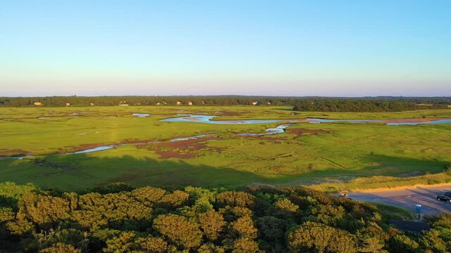 Drone aerial of coastal marshland with river-like bends and tidal creeks cutting through bright green grasses. Peaceful nature scenery, wide panorama, cinematic 4K b-roll.