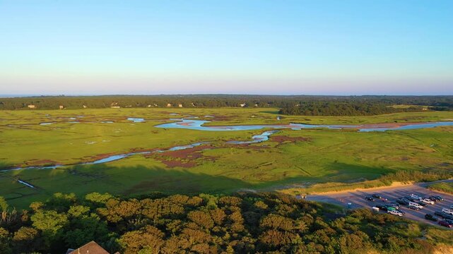 Drone aerial over winding salt marsh channels and green wetlands in warm golden light. Calm coastal landscape with meandering creek reflections and wide horizon, cinematic 4K b-roll.