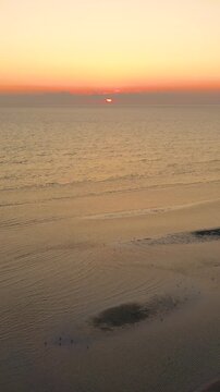Vertical drone sunset along Nantucket shoreline, golden light on calm sea with winding sandbars and tidal pools. Tall coastal evening panorama, peaceful stock footage.
