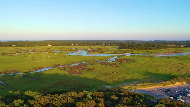 Drone aerial over Cape Cod salt marsh with sweeping creek bends and lush coastal wetlands glowing at golden hour. Serene New England landscape, smooth cinematic 4K b-roll.