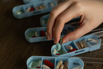 Fototapeta premium Person organizing pill boxes by day of the week for medication management on a wooden table