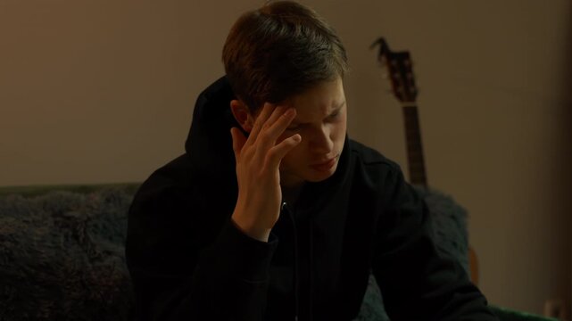 A guy having a headache while seated on a couch, massaging his temple, closeup