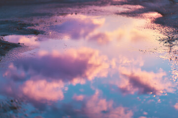 Pastel reflections in a puddle capture the warm glow of summer sky colors at dusk, creating a nostalgic view of the world below and a soft dreamy atmosphere