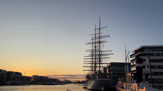 Sunset view over Bremerhaven harbor with calm water, historic sailing ship silhouettes and modern waterfront buildings under a clear evening sky.