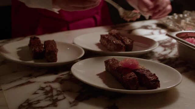 A professional chef carefully arranges and garnishes succulent grilled meat kebabs on white plates in a high-end restaurant kitchen.