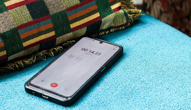 Voice detection and recording app in mobile phone listening to contestation laying on couch or sofa hidden from view. Secretly grabbing and wiretapping inside home or apartment during covert operation
