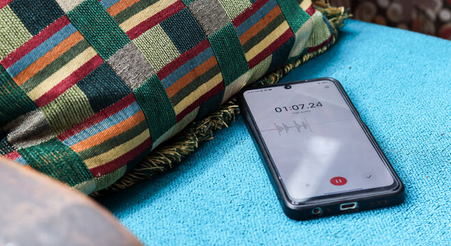 Voice detection and recording app in mobile phone listening to contestation laying on couch or sofa hidden from view. Secretly grabbing and wiretapping inside home or apartment during covert operation