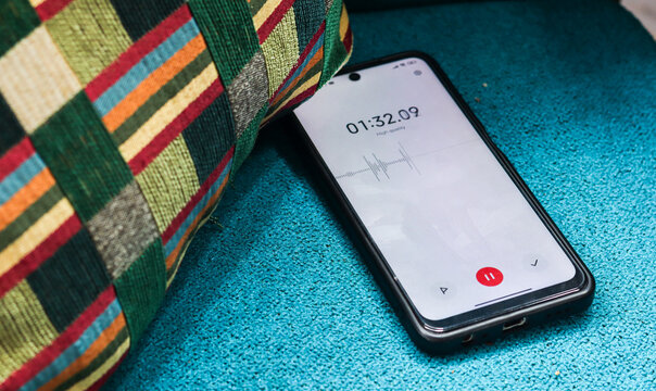 Voice detection and recording app in mobile phone listening to contestation laying on couch or sofa hidden from view. Secretly grabbing and wiretapping inside home or apartment during covert operation