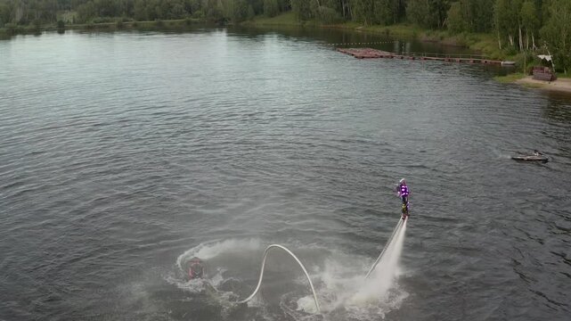 Flyboard show on open water. Athlete man performs tricks in the air over a picturesque lake. Spectacular sports. Extreme lifestyle and water activity.