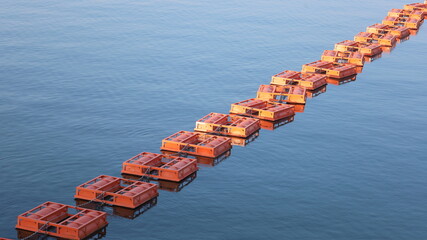 Line of buoys on the surface of the water. Close-up of row of orange floating metal buoys in dam marking safety danger zone on blue water background with selective focus. © kanin