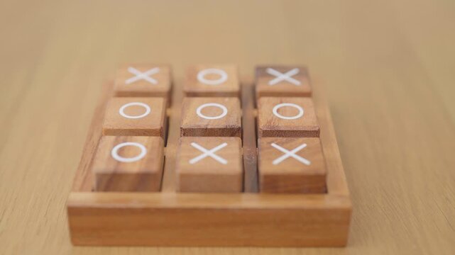 Hand holding and playing wooden block of tic tac toe game. A completed game of noughts and crosses or Xs and Os game. Challenge, Competition, winning, tactic, strategy and recreation concepts