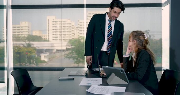 Young businesswoman looking at laptop while male colleague explains strategy during meeting. Cooperative startup office scene showing collaboration and business development focus