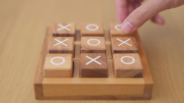 Hand holding and playing wooden block of tic tac toe game. A completed game of noughts and crosses or Xs and Os game. Challenge, Competition, winning, tactic, strategy and recreation concepts