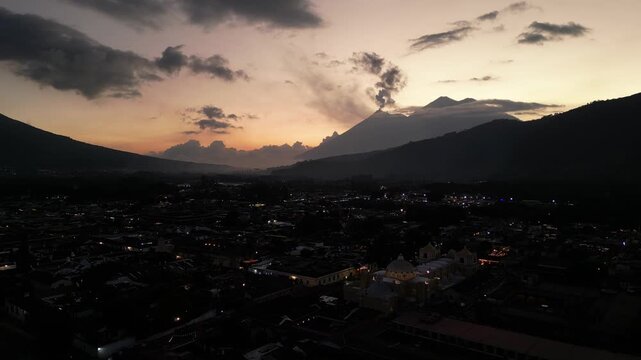 antigua guatemala sunset (scenic view of fuego acatenango volcanic eruption with cloud formation merced church agua) nightfall night time cityscape aerial drone view colorful sky volcanic highlands