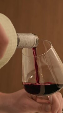 Vertical shot of hands of unrecognizable man filling glass with red wine from bottle in home kitchen