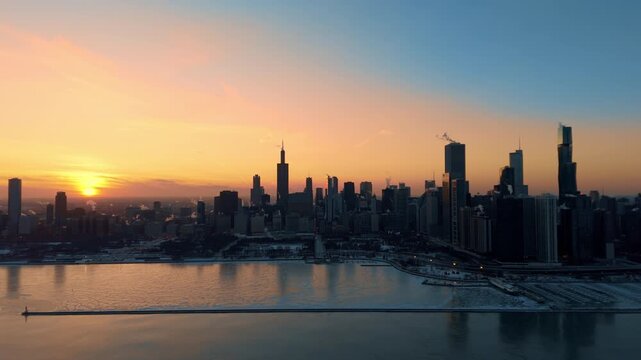 Drone view of downtown Chicago skyline at sunset during winter. The surface of Lake Michigan as subzero temperatures create frozen patterns along the shoreline