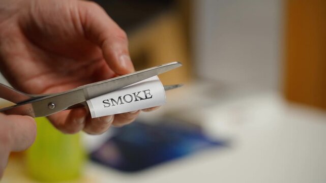 Scissors cutting out a sticker with the word SMOKE, close-up in slow motion