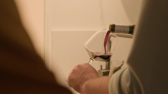 Close up shot of hands of unrecognizable man pouring glasses with red wine while having romantic date with girlfriend at home