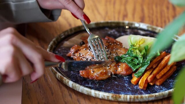 Detailed view of gourmet chicken garnished with sweet potato and pak choi being eaten with fork at restaurant table. Focus on texture and freshness, premium dining experience, food enjoyment concept.