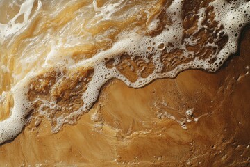 Obraz premium Closeup view of sandy beach covered in small waves with rich textures and foam during sunlight reflecting on the water at a coastal location