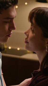 Vertical shot of tender young couple looking into each others eyes while slow dancing at home under warm light