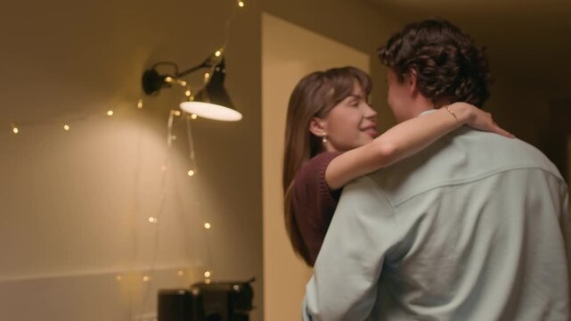 Medium shot of happy young Caucasian man and woman looking at each other while enjoying dance during home evening