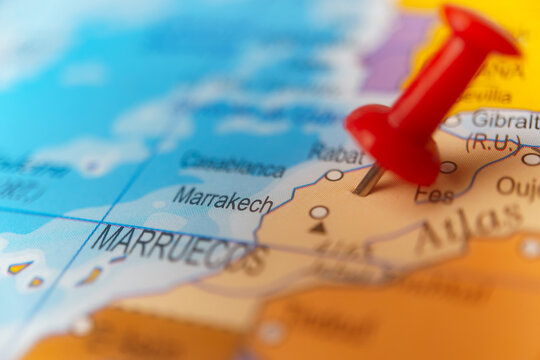 Red pushpin pointing to fes on a physical world map, indicating travel destination or specific location in morocco