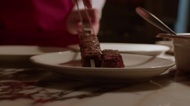 A detailed close-up shot of a chef using metal tongs to carefully place juicy grilled meat skewers onto a clean white plate in a restaurant kitchen