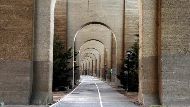 view of bike lane under stone railway bridge trestle in randall's island queens new york city (hell's gate arches brick archway public park) pedestrian cycling path nyc biking scenic infrastructure
