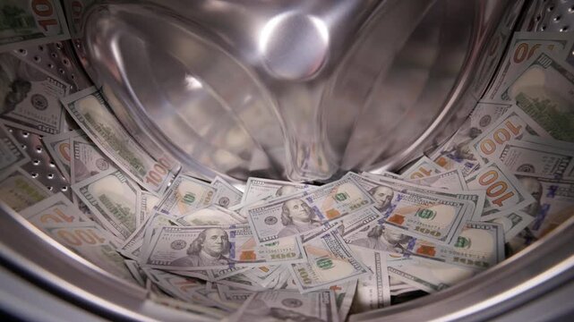 Hand throwing US dollar banknotes in a washing machine, money laundering concept.