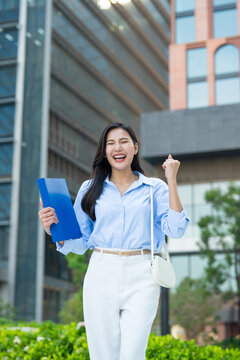 Portrait of Asian excited businesswoman looking at camera outdoors in city. 