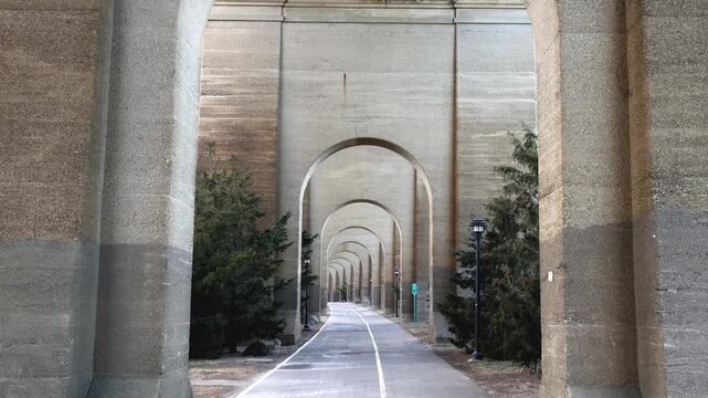 view of bike lane under stone railway bridge trestle in randall's island queens new york city (hell's gate arches brick archway public park) pedestrian cycling path nyc biking scenic infrastructure