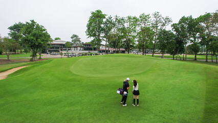 Drone view of male and female golfers walk across lush green fairway. 