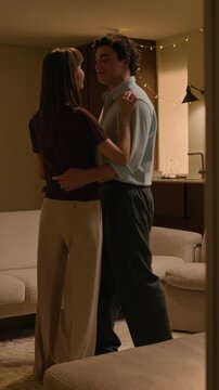 Vertical shot of elegant young boyfriend and girlfriend enjoying dance in cozy living room with warm lighting