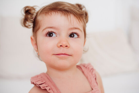 Smiling toddler with hair buns indoors showing innocence and curiosity