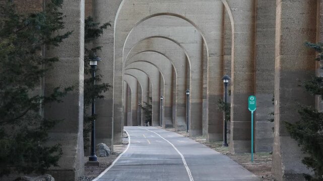 view of bike lane under stone railway bridge trestle in randall's island queens new york city (hell's gate arches brick archway public park) pedestrian cycling path nyc biking scenic infrastructure