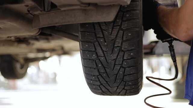 Mechanic rotating car winter tire in garage workshop environment.