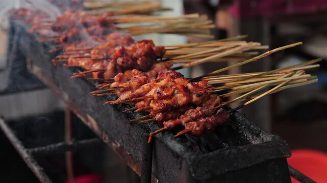 Indonesian chicken satay skewers grilling over hot charcoal with smoke for street food concept