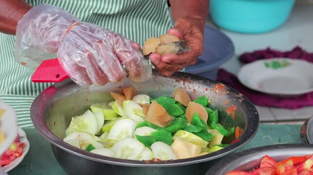 Indonesian street food vendor preparing traditional snack with cucumber and sauce for culinary concept