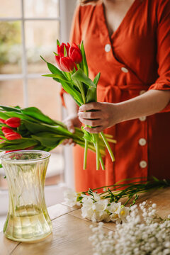 Woman in orange dress arranging tulip and gypsophila bouquet at home