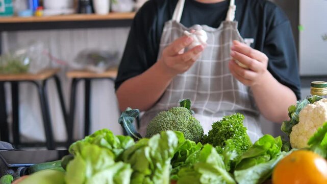 Person preparing fresh vegetables with garlic on kitchen table. Home cooking, healthy meal preparation and clean eating concept