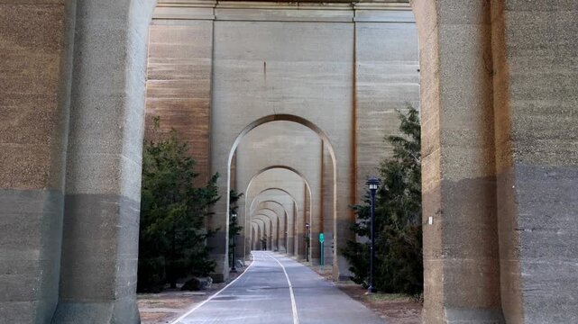 view of bike lane under stone railway bridge trestle in randall's island queens new york city (hell's gate arches brick archway public park) pedestrian cycling path nyc biking scenic infrastructure