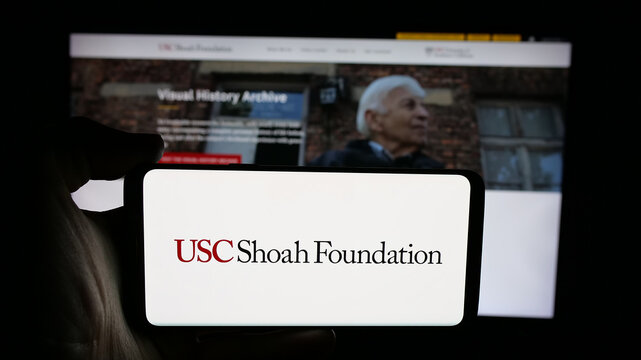 Stuttgart, Germany - 01-30-2026: Person holding cellphone with logo of US organisation USC Shoah Foundation on screen in front of webpage. Focus on phone display.