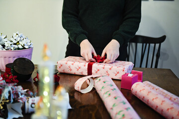 Obraz premium Person attaching red bow to wrapped gift on wooden table.