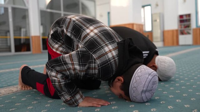 Two Muslim boys in sujud prostration during prayer at a mosque. Young children performing Sajda in spiritual devotion. Muslim kids learning to pray at masjid during Ramadan.