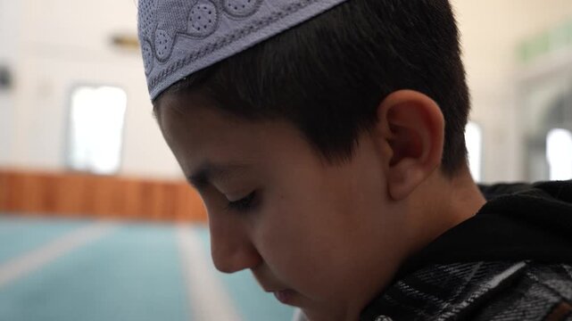 Muslim boy making Dua and praying in a mosque with devotion. Young child supplicating during Ramadan at masjid. Muslim kid praying with hands raised in a spiritual moment.